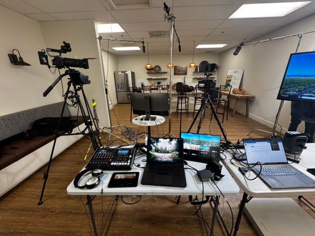 Professional video production setup with multiple monitors, cameras, and lighting equipment arranged on wooden desks.