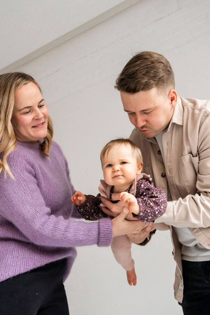 Hauska perhekuva, toiminnan kautta otettu kuva, vanhemmat lennättää lasta, kuvattu alaviistosta.