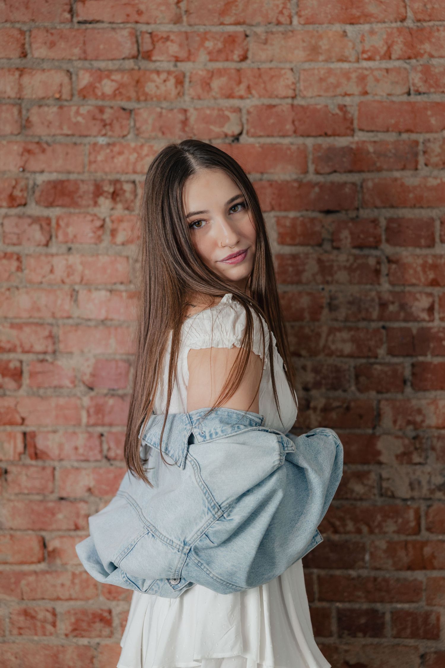 Fashion portrait against rustic brick wall featuring light denim jacket and white lace top.