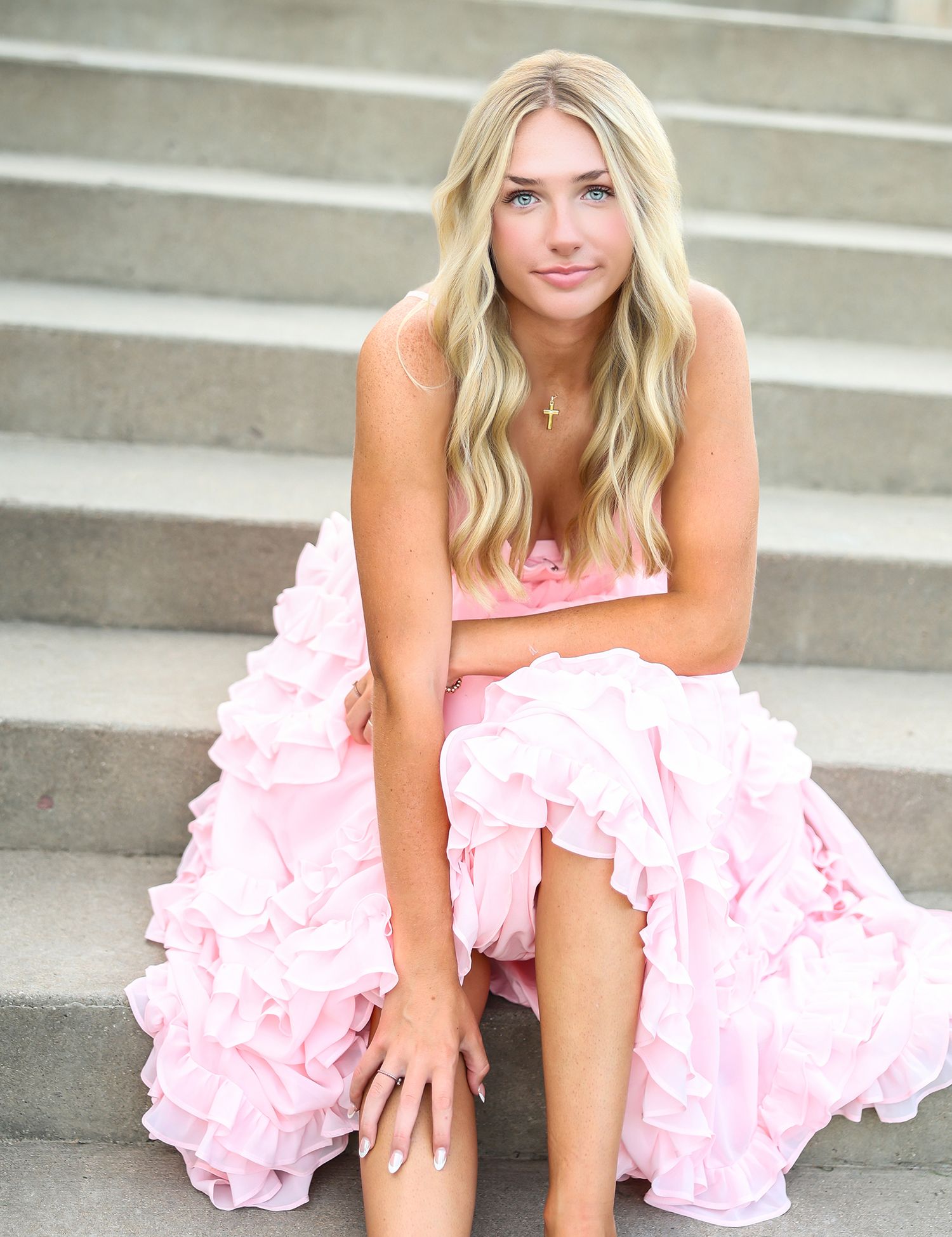 Elegant portrait on concrete steps wearing a pink ruffled dress.