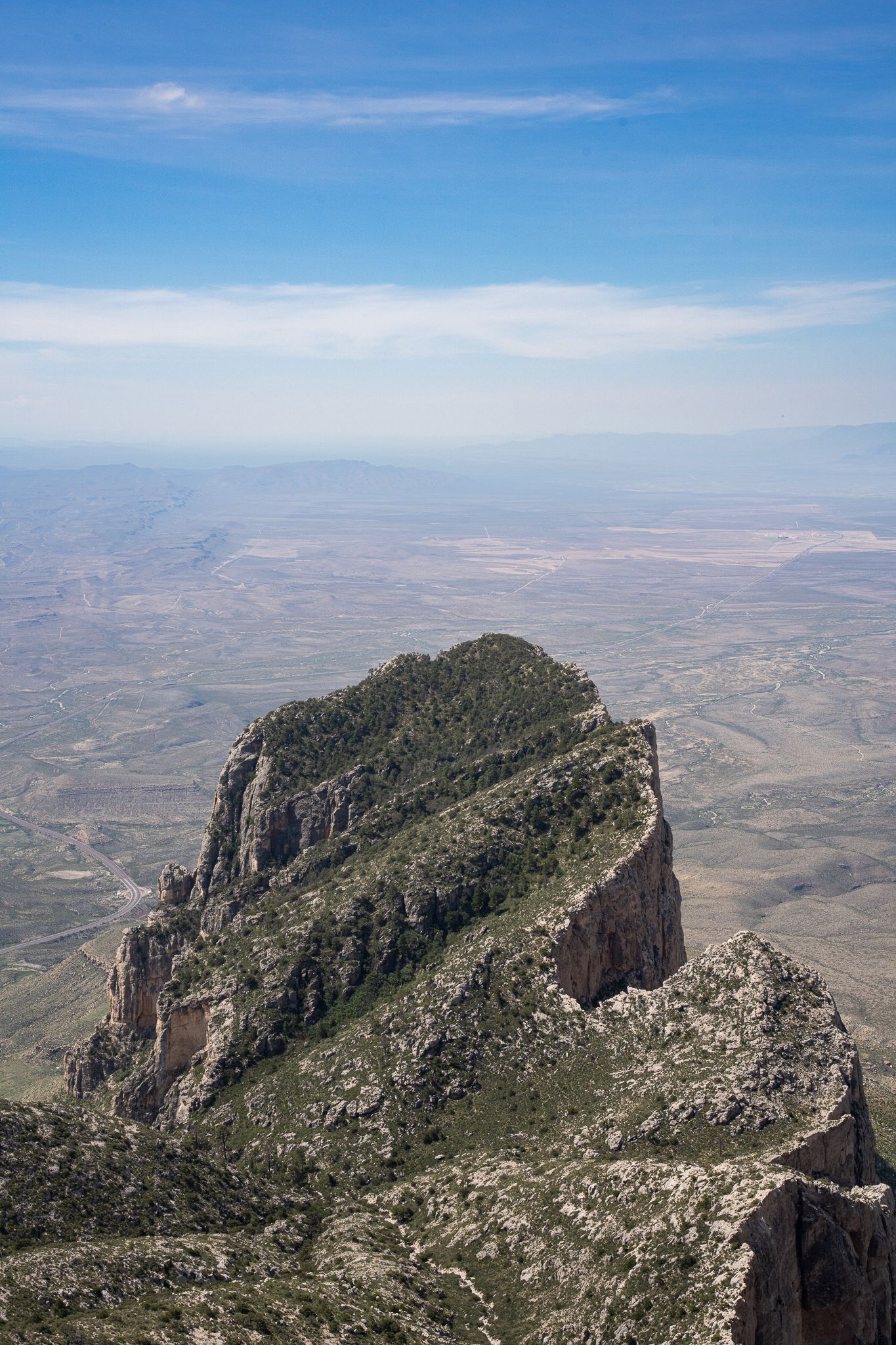 Rugged mountain peak rises dramatically above desert landscape under bright blue sky in Guadalupe Mountains National Park.