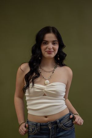 A series of photos showing someone in a white crop top and jeans posing against a dark green background. Headshot, branding photos, senior