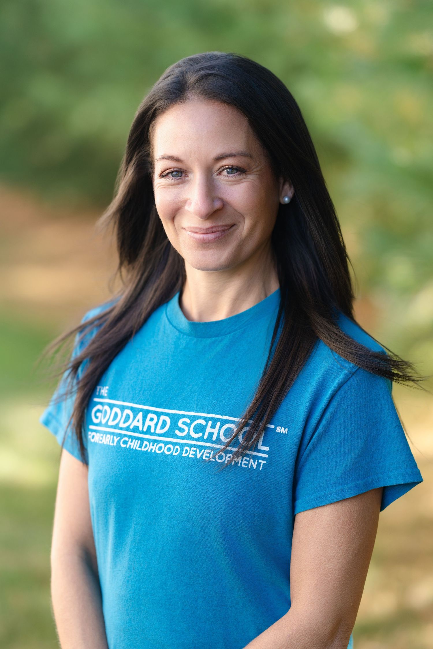 Person wearing bright blue Goddard School t-shirt smiling in outdoor setting.