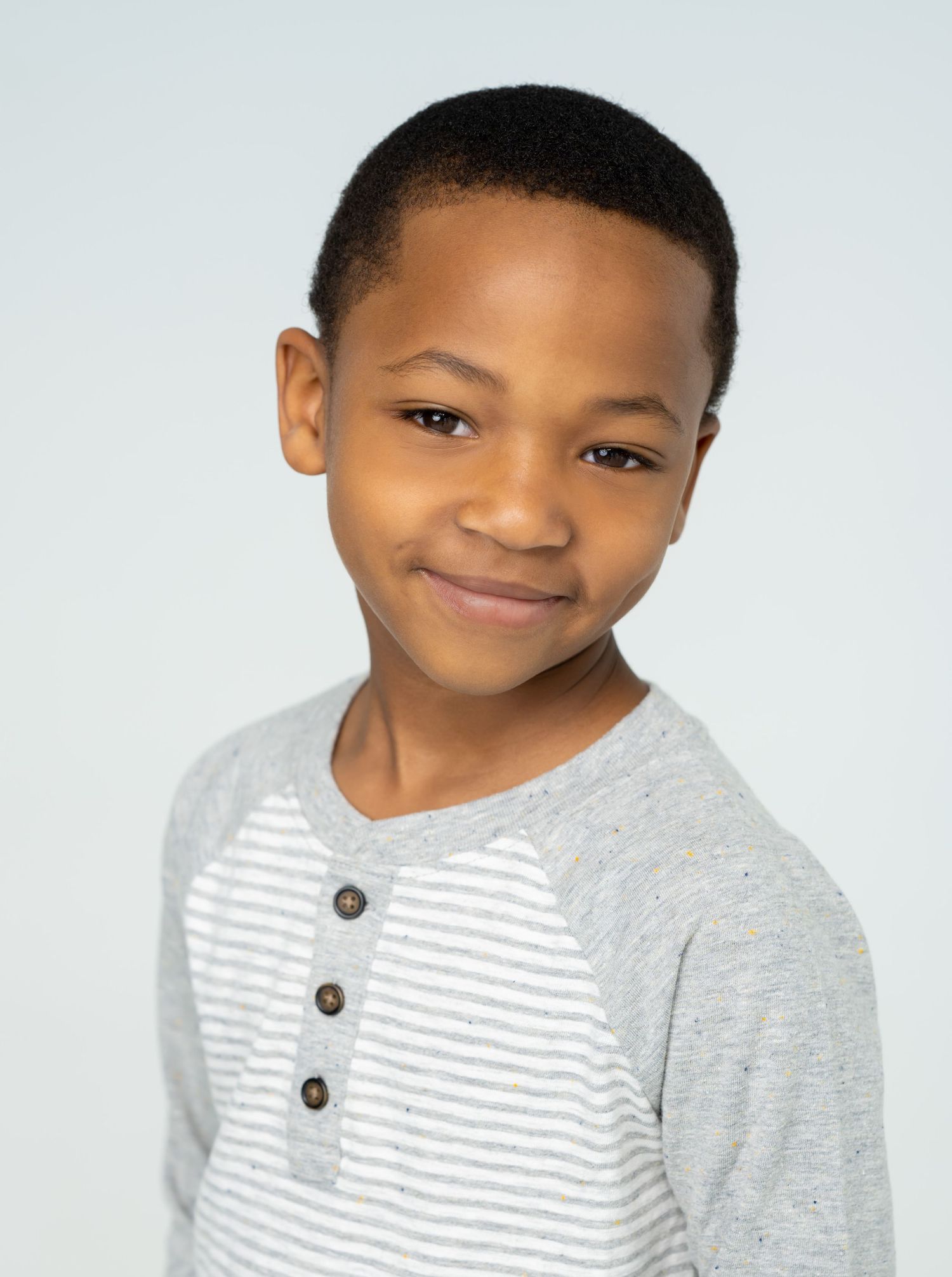 Studio portrait of child wearing grey and white striped henley shirt.