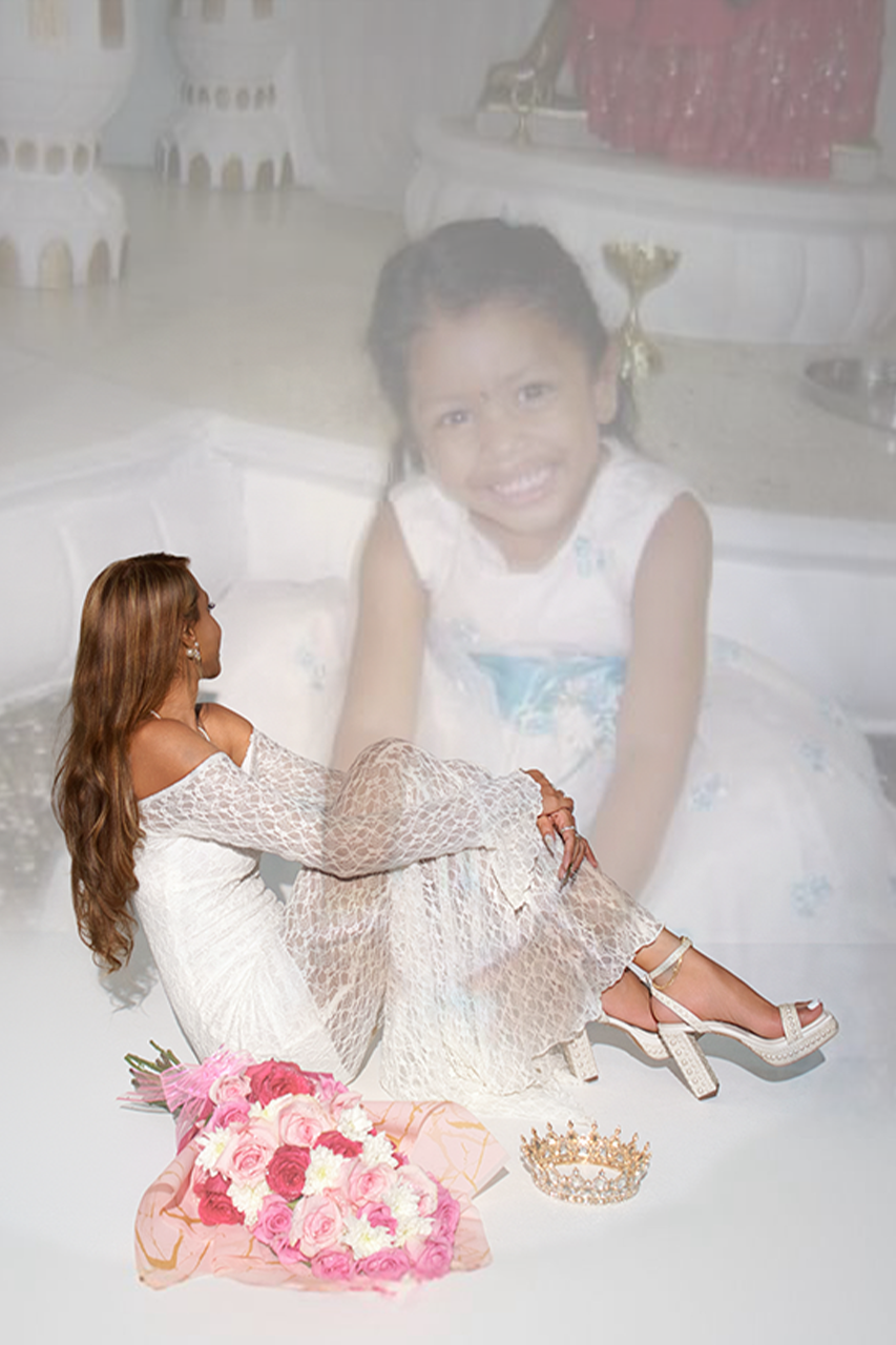 A person in a white dress lies on the floor surrounded by pink floral decorations in a dreamy photoshoot setting.