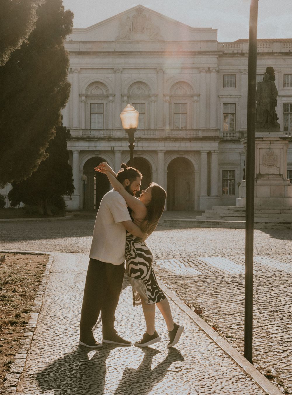 A couple dances in golden sunlight on cobblestone streets.