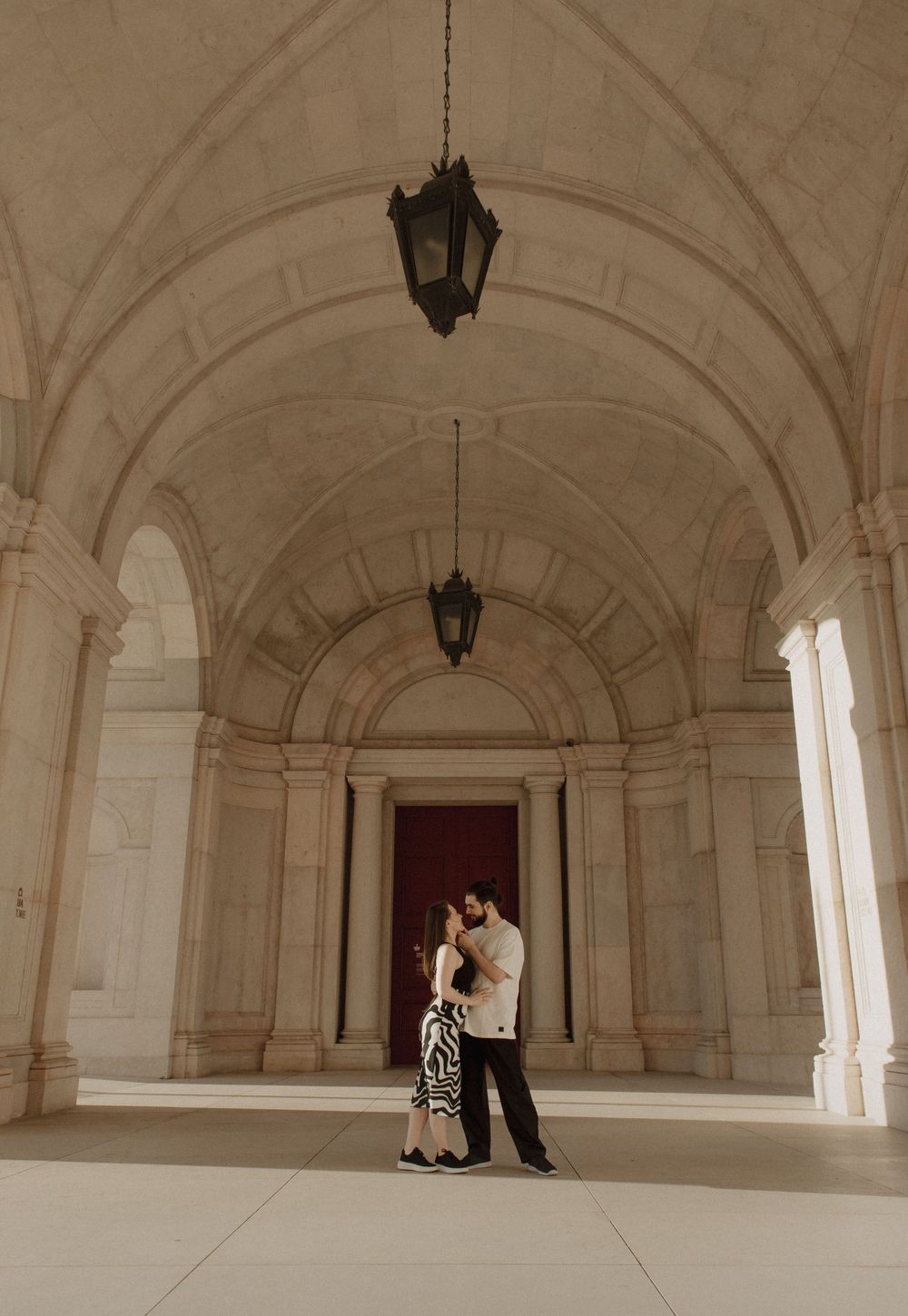 Wide architectural shots showing couple's intimate moments in grand arched hallway.