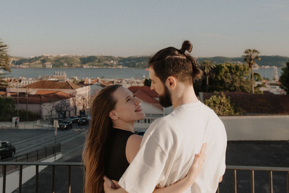A couple embraces on a rooftop terrace overlooking a scenic coastal bay during sunset.