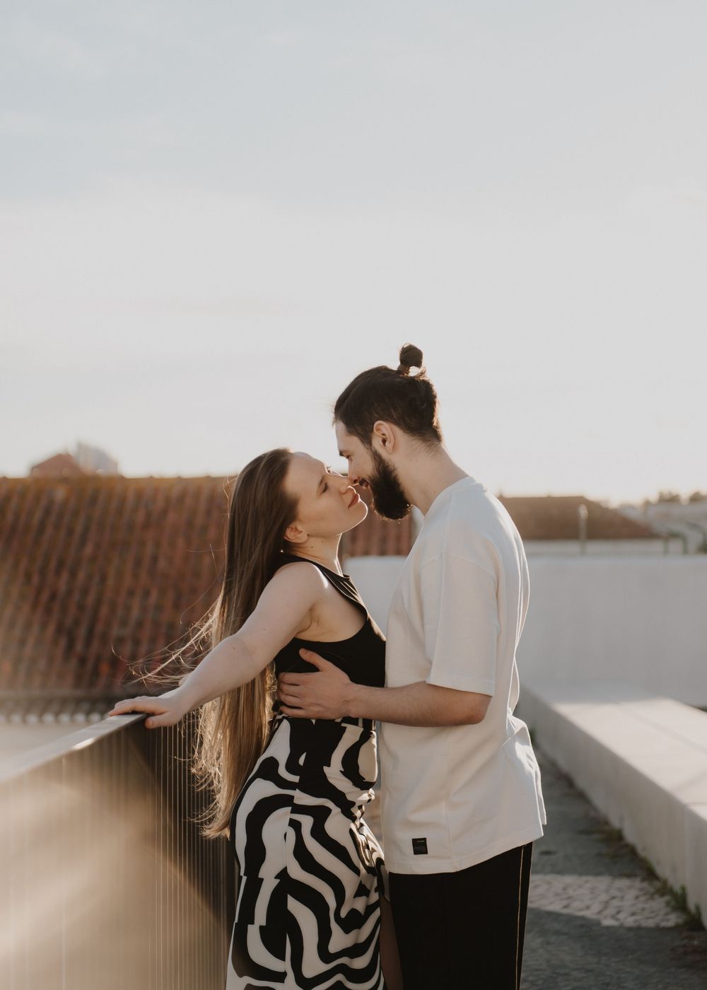 A romantic couple embraces on a rooftop during golden hour with soft sunlight creating a dreamy atmosphere.