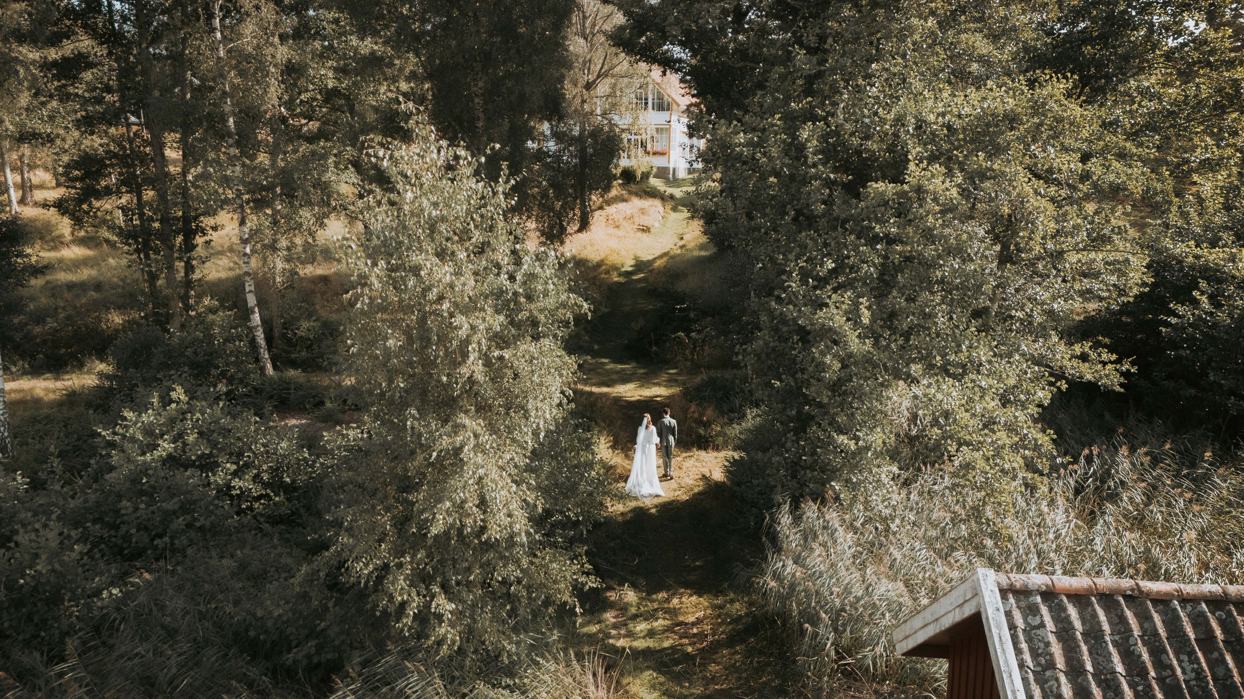 Panoramic view of a rustic outdoor wedding venue with stone buildings and natural landscaping.