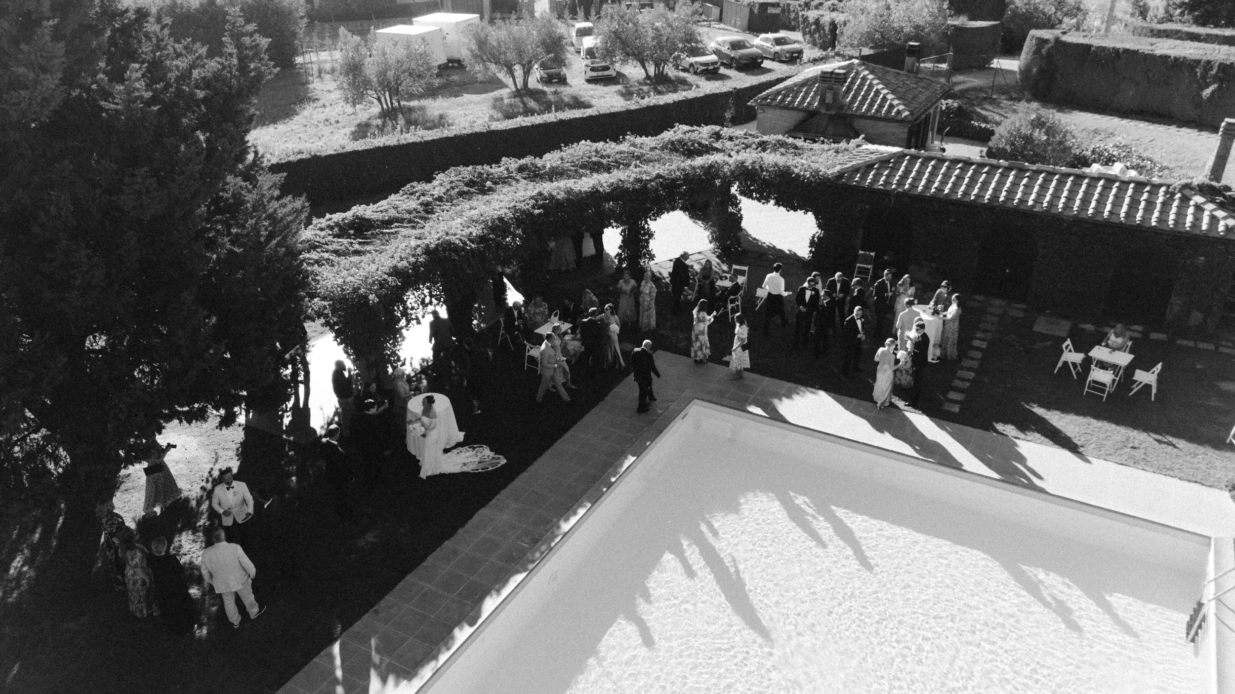 Black and white panoramic shot of wedding guests gathering at an outdoor reception venue.