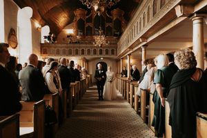 Wedding ceremony in progress inside a traditional church with wooden pews and balcony.