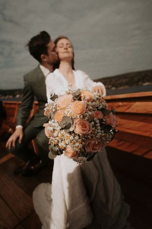 Romantic peach and blush wedding bouquet displayed against wooden backdrop.