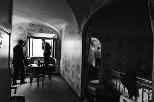 Moody black and white photograph of figures in an arched hallway interior.