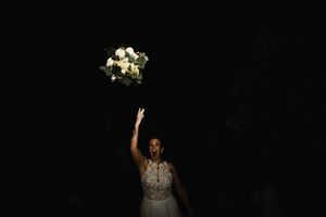 Dramatic silhouette of someone tossing a wedding bouquet against a dark background.