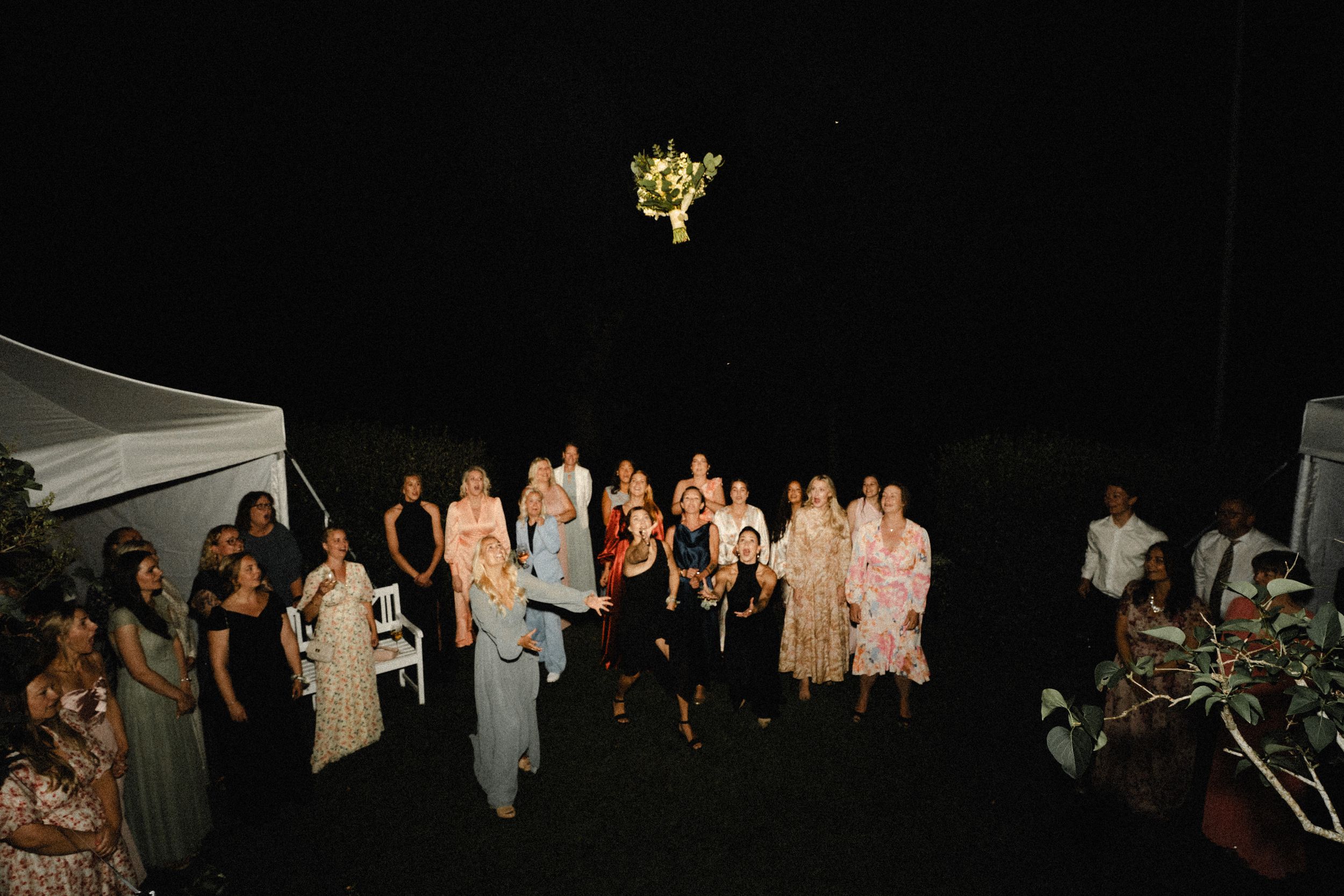 Wedding guests gather for a nighttime celebration under twinkling lights and a glowing chandelier.