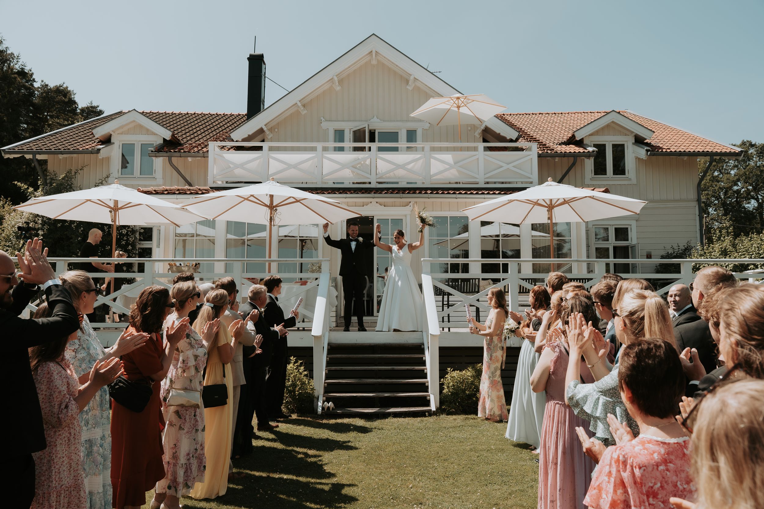 Wedding party celebrating outdoors under white tents and blue skies on a sunny day.