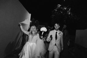 Newlyweds exit their celebration carrying bouquets in a black and white capture.