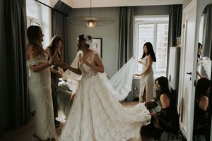 Wedding preparation scene with flowing white dress being arranged in a modern hotel room.