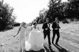 Wedding party walking and laughing together on a sunny hillside path.