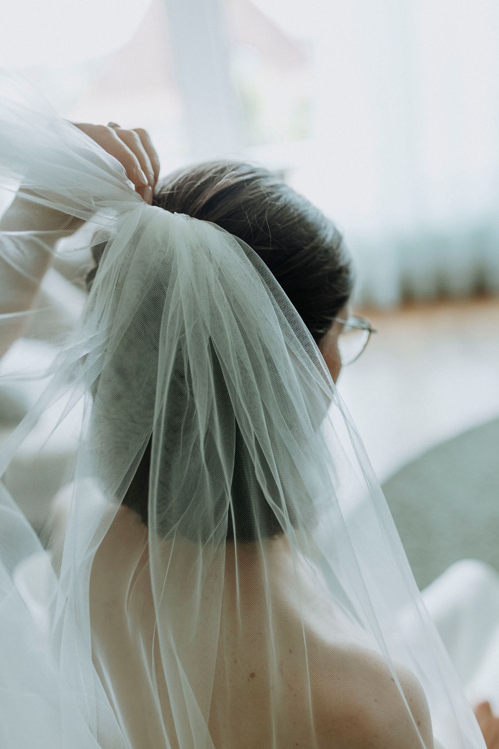 Delicate white wedding veil being adjusted in soft natural light.
