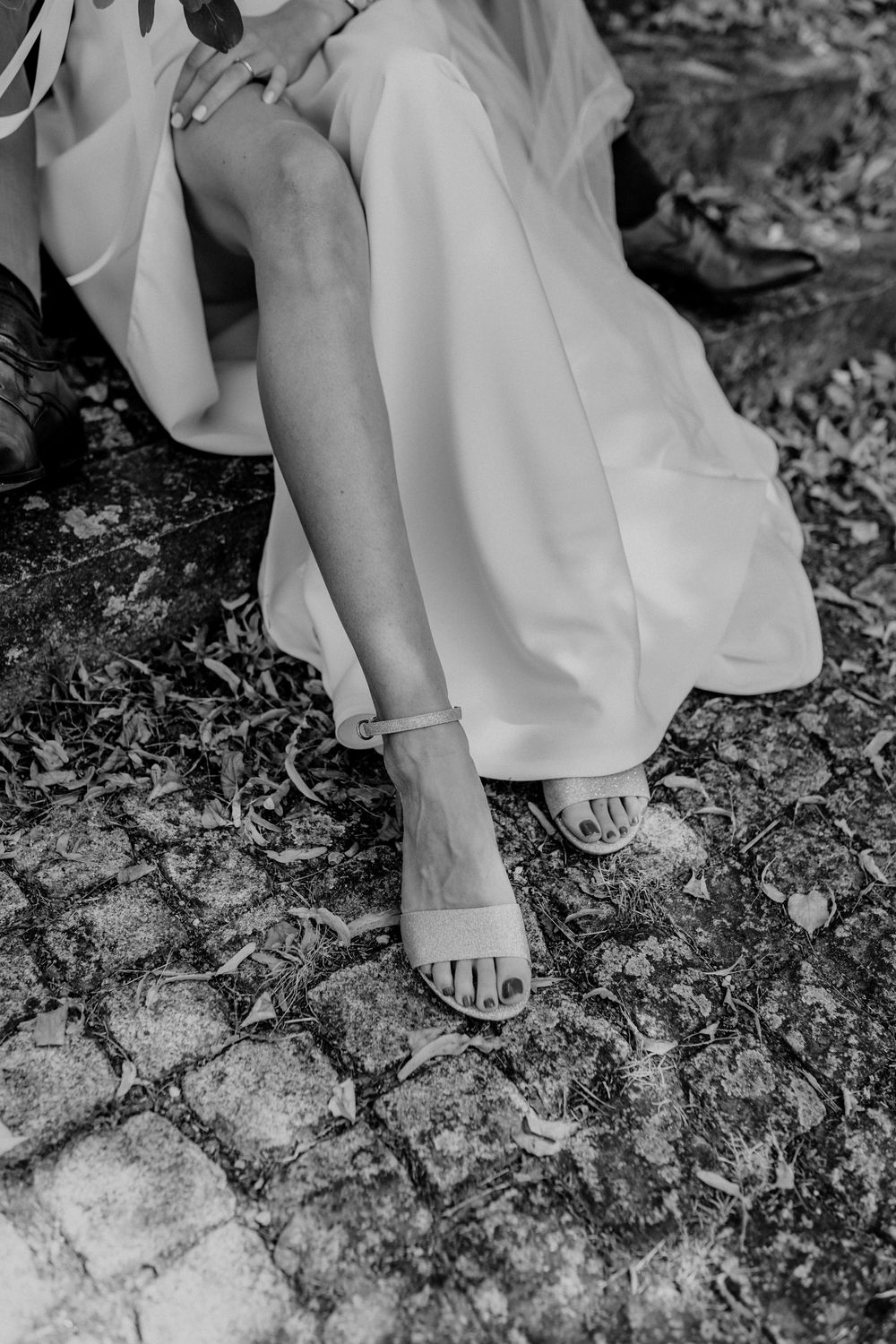 Close-up of bridal shoes and wedding dress hem on natural stone ground.