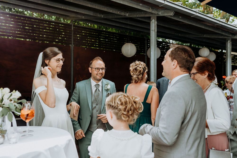 Wedding guests mingling at an outdoor reception with white decor and grey suits.