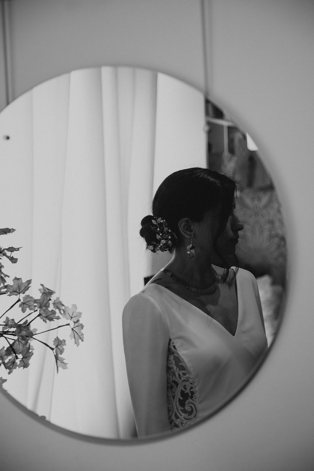 Black and white reflection of bride in elegant updo and white gown in a round mirror.
