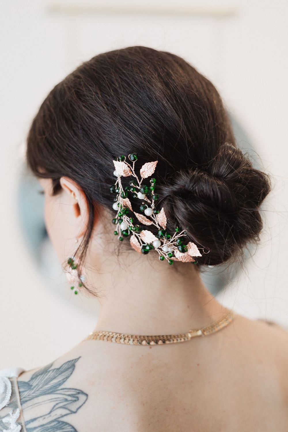 Close-up of bridal updo adorned with rose gold leaf and green bead hair accessory.