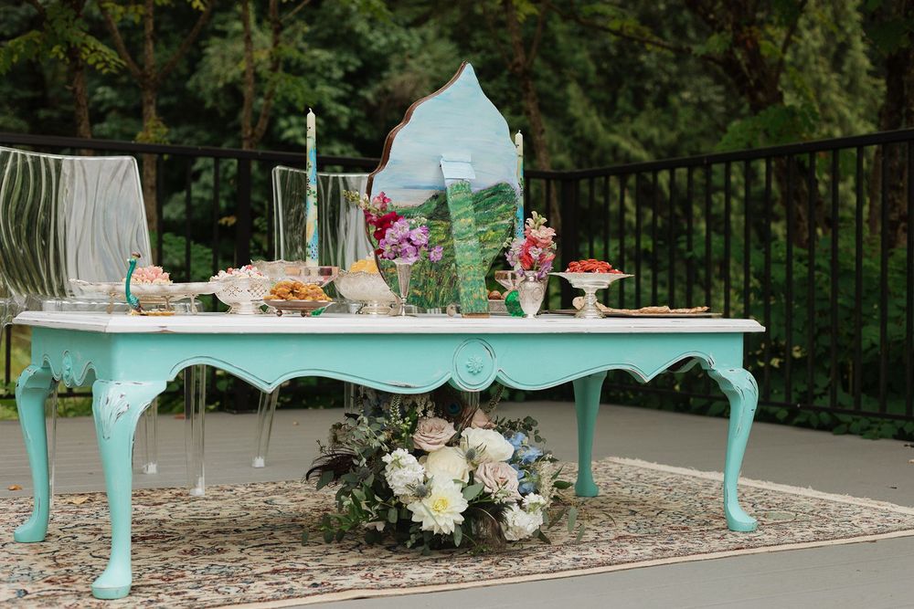 Elegant turquoise vintage table styled as a wedding dessert display with flowers and candles outdoors.