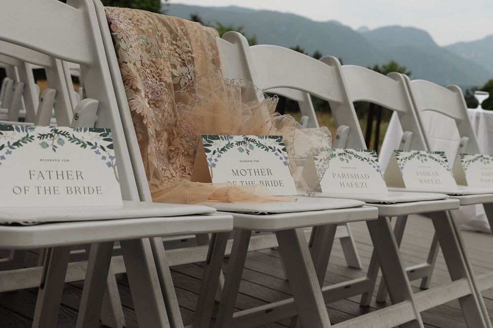 White wedding ceremony chairs labeled Father of the Bride and Mother of the Bride in a row.