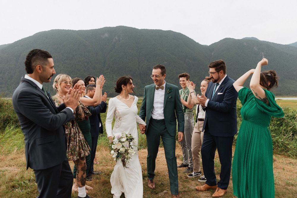 Bride and groom celebrate with cheering guests against a stunning mountain backdrop outdoors.