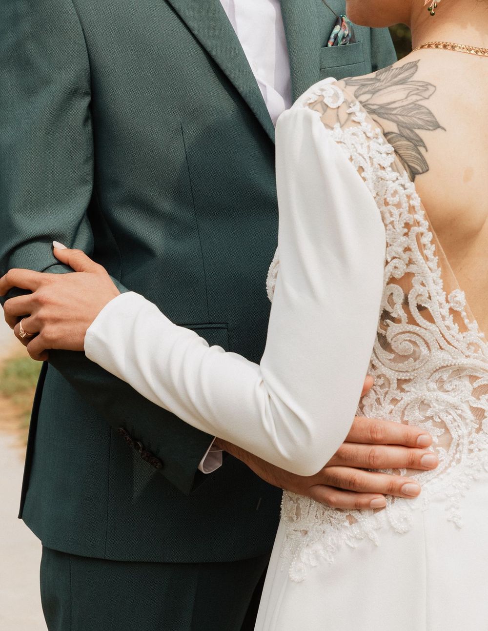 Close-up of bride in lace back wedding gown embracing groom in dark green suit.