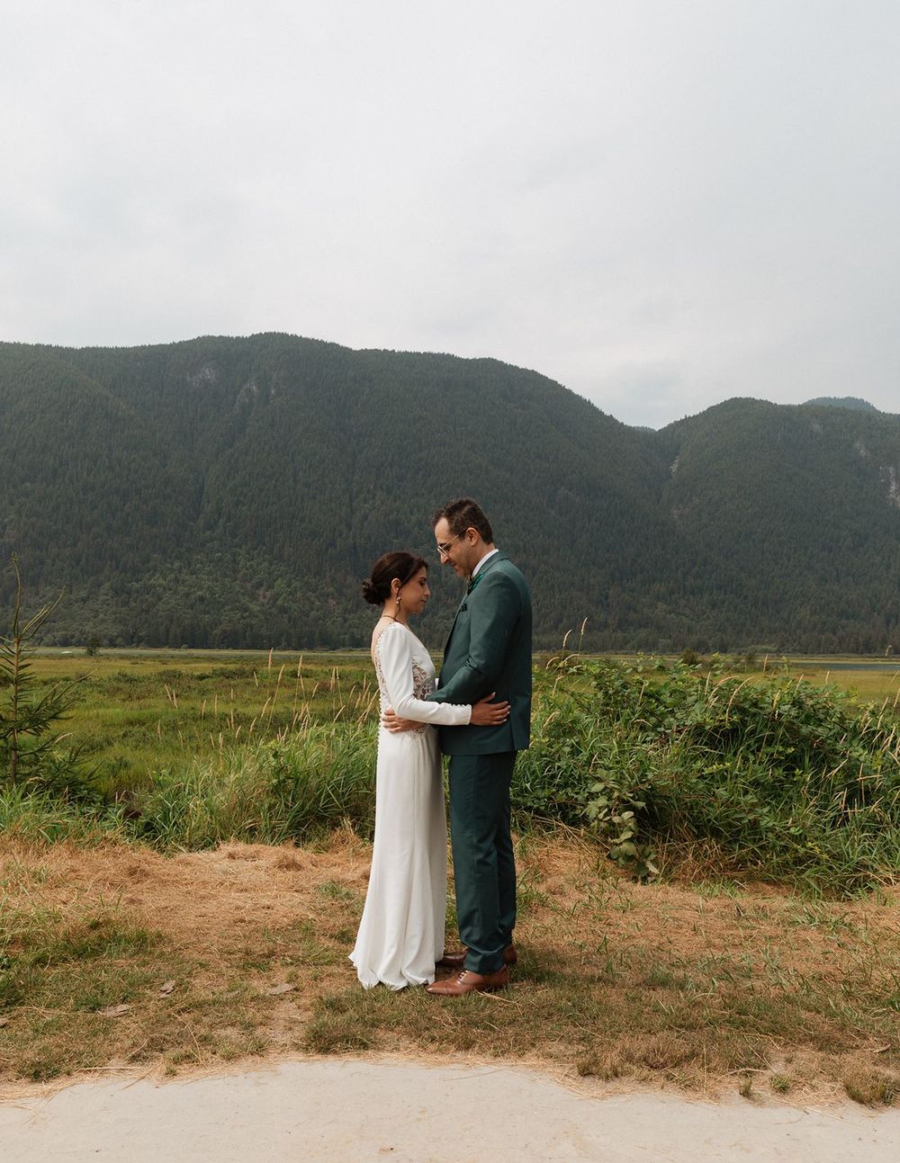 Bride and groom share an intimate moment on a dirt path with stunning mountain and valley backdrop.