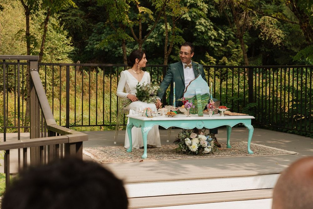 A bride and groom stand at a mint green table during an intimate outdoor wedding ceremony on a patio.