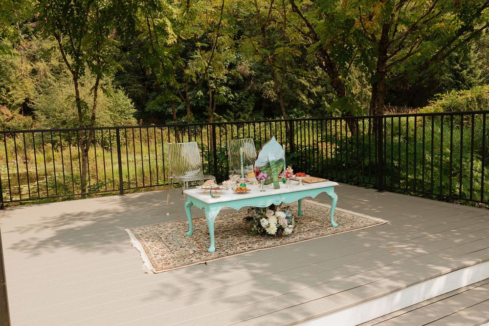 A decorated mint green vintage table with floral arrangements set on a patio surrounded by lush greenery.