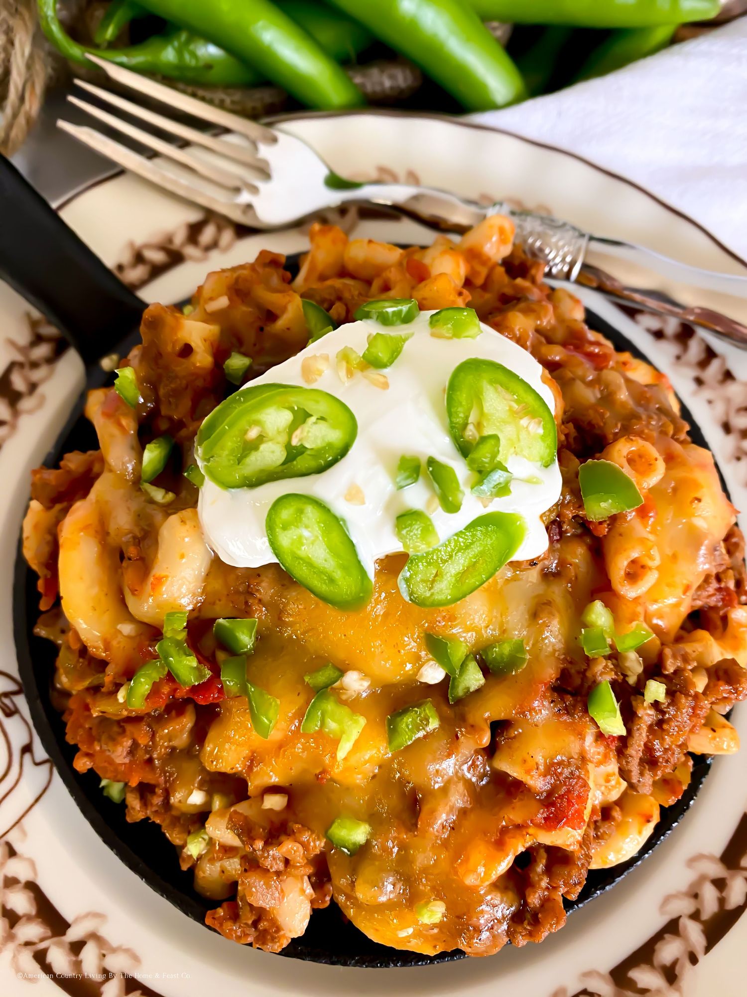 Mexican-inspired taco casserole topped with melted cheese, sour cream, and sliced jalapenos on a decorative plate.
