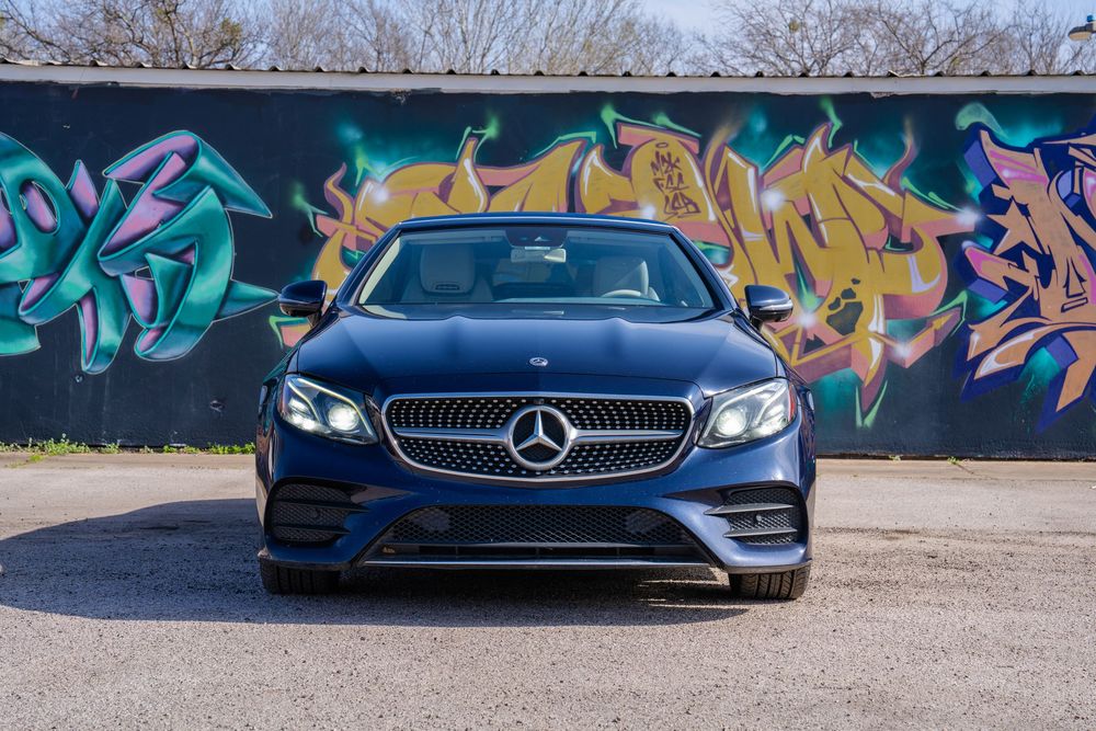 A sleek black Mercedes-AMG GT sports car parked in front of a vibrant graffiti wall with colorful artwork.