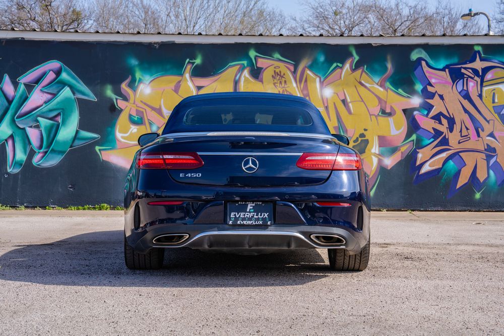 A dark blue Mercedes-Benz C63 AMG coupe parked in front of a colorful graffiti wall.