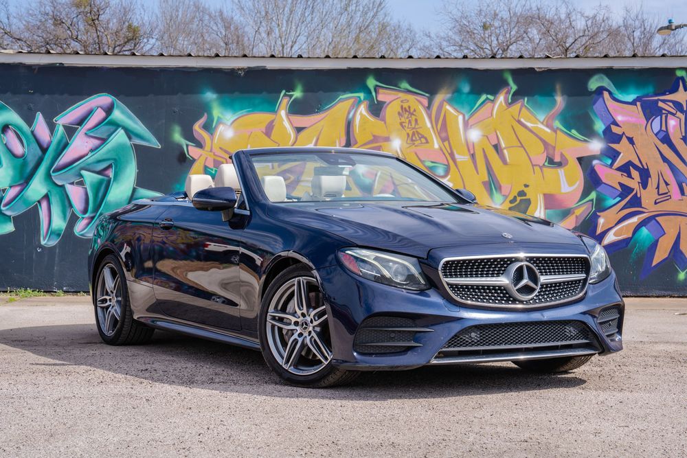 A blue Mercedes-Benz sports car parked in front of a vibrant graffiti wall showcasing colorful street art.