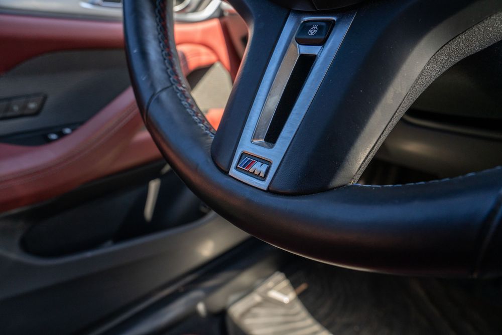 Interior view of a modern car dashboard showing leather trim, steering wheel, and digital displays in dark lighting.