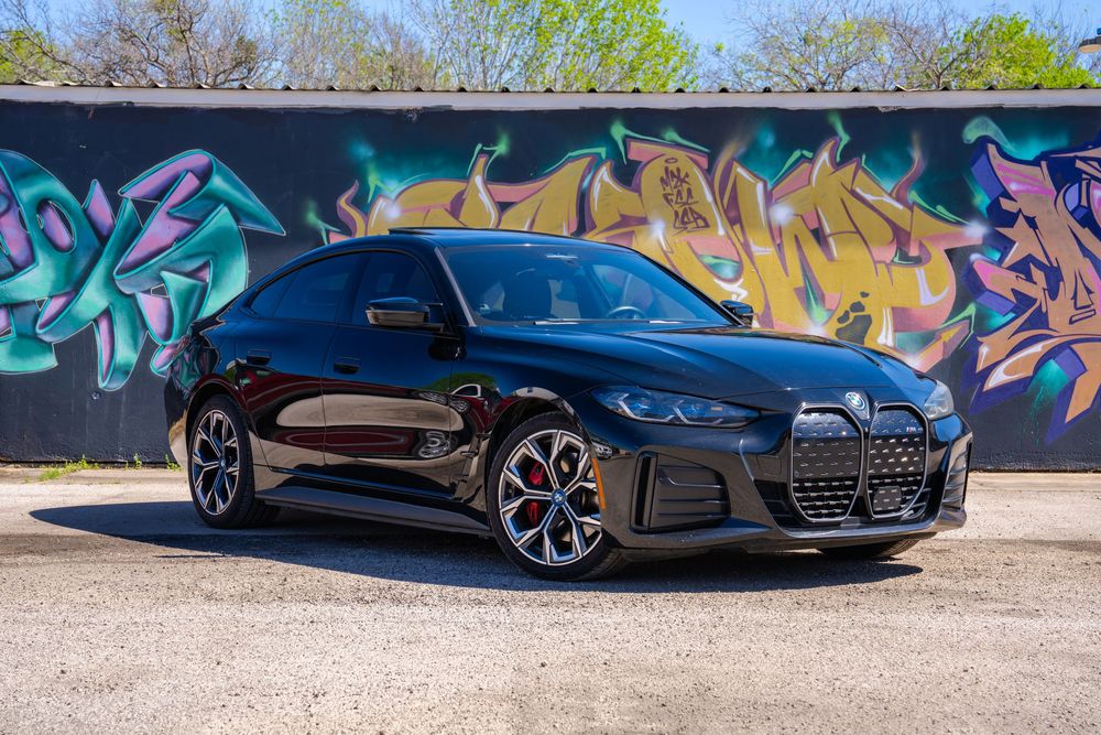 A sleek black Audi R8 sports car parked in front of a colorful graffiti wall on a sunny day.