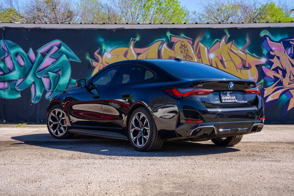 Black Aston Martin sports car parked in front of colorful graffiti wall on a sunny day.