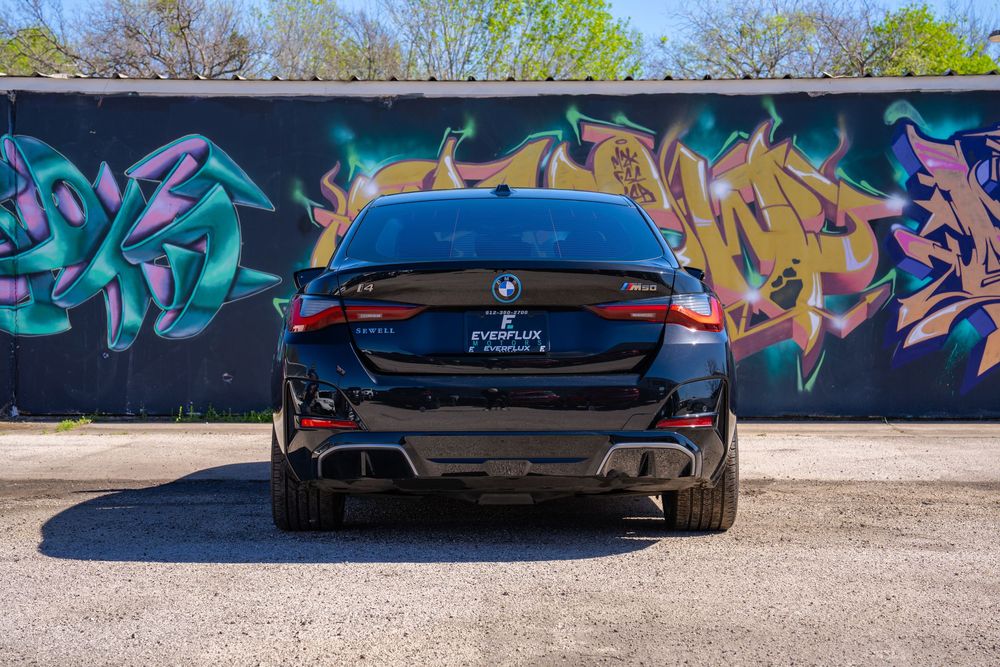 Black sports car parked in front of colorful graffiti wall with abstract designs and vibrant colors.