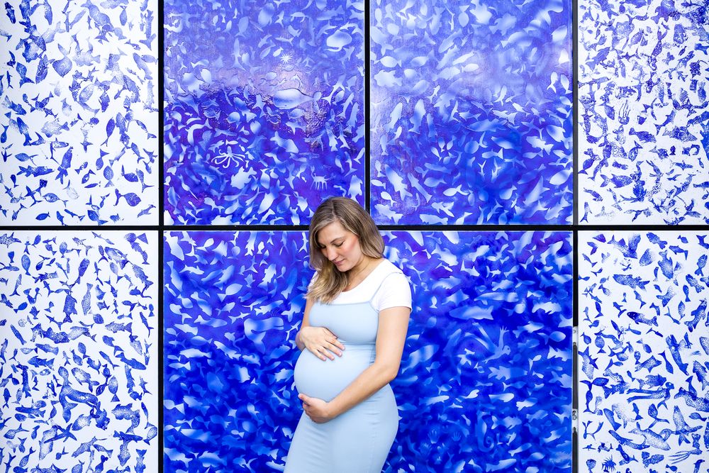 pregnant woman in light blue dress posing in front of deep blue painted wall st Katharine docks