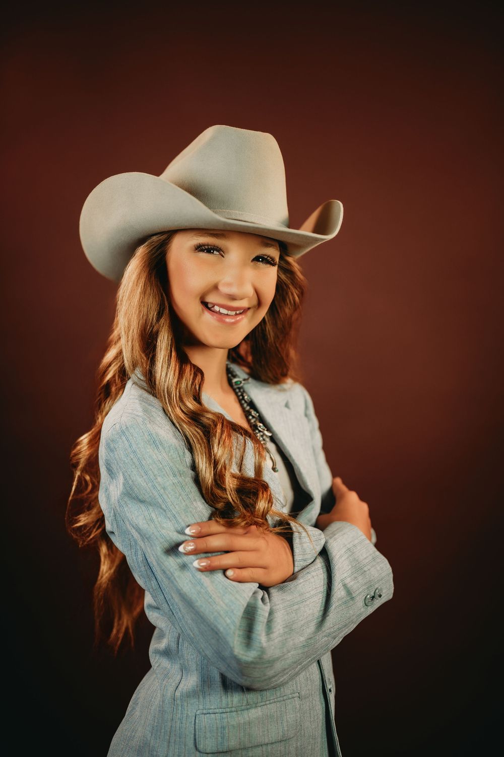 Western style portrait with light denim jacket and white cowboy hat against brown backdrop.