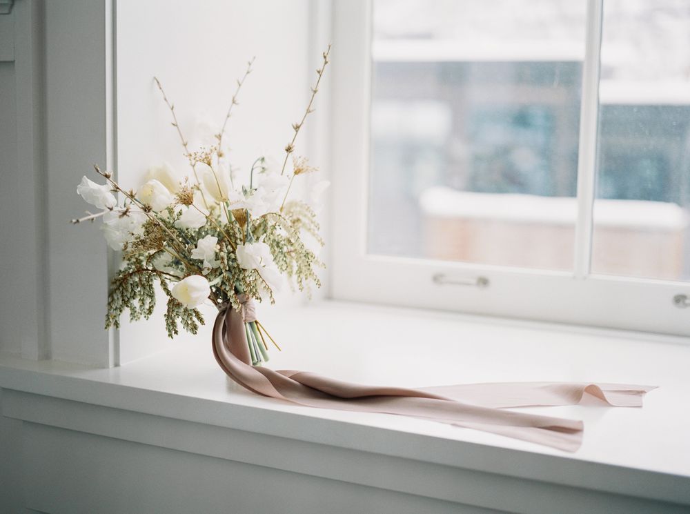 White flowers in a vase sit on a windowsill with natural light streaming through the window.