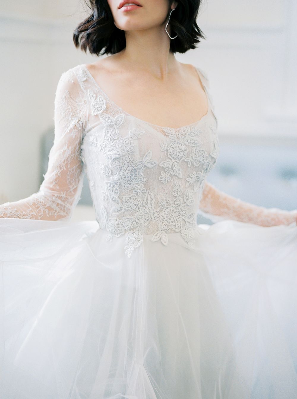 A romantic white lace wedding dress with sheer long sleeves and tulle skirt shown in a series of ethereal photos.