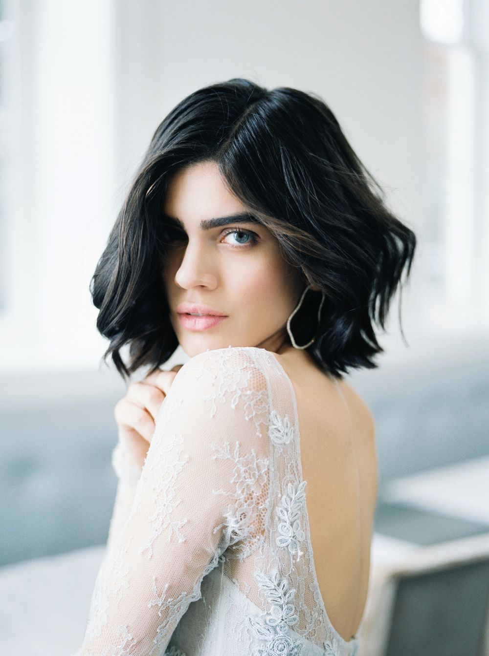Portrait showing dark wavy bob haircut and delicate lace sleeve against soft natural lighting.