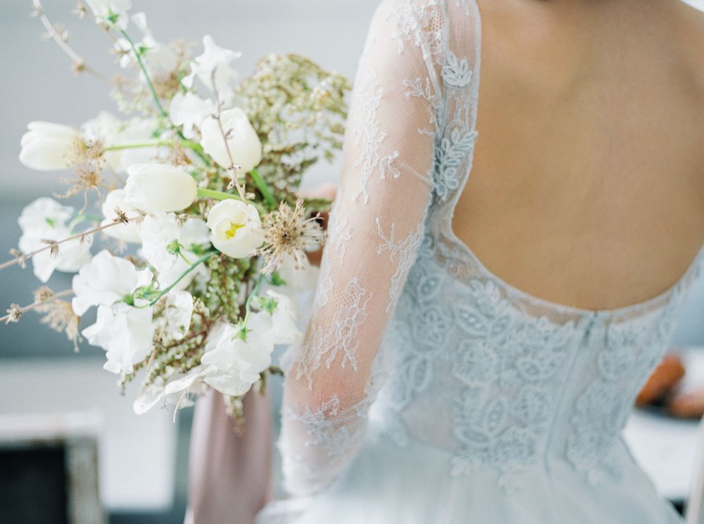A close-up detail shot of delicate white lace on a wedding dress with floral embroidery and beading.